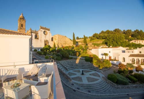 Vista de la terraza de Casa La Muralla en Medina Sidonia con tumbonas blancas, torre de iglesia histórica y anfiteatro morisco