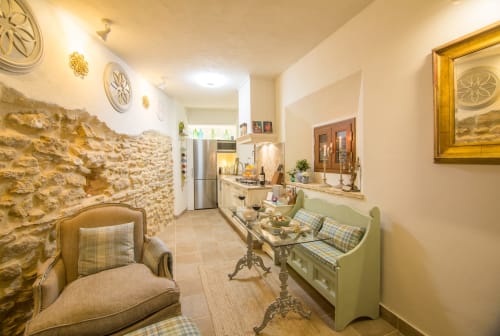 Acogedor estar en la casa rural Casa La Muralla, Medina Sidonia, con paredes de piedra, sofá verde, sillón y cocina abierta