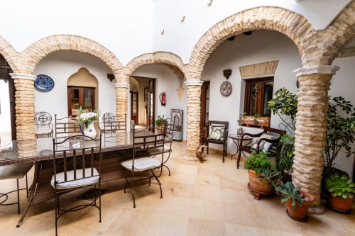 Patio andaluz con arcos de ladrillo, azulejos de terracota, puertas de madera y plantas en macetas en Casa de Medina, Medina Sidonia