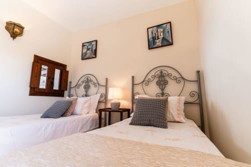 Dos camas con cabeceros de hierro forjado ornamental en la Casa de Medina, villa Medina Sidonia, dormitorio con paredes color crema y obras enmarcadas