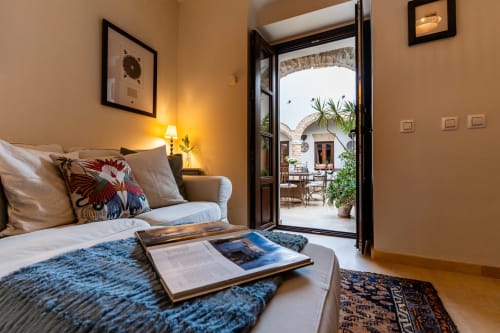 Dormitorio con puertas abiertas al patio andaluz, ropa de cama azul, lámpara y cojines en Casa de Medina, Medina Sidonia