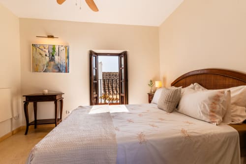 Dormitorio luminoso en la Casa de Medina, Medina Sidonia, con cama de madera, puertas al balcón y decoración neutral