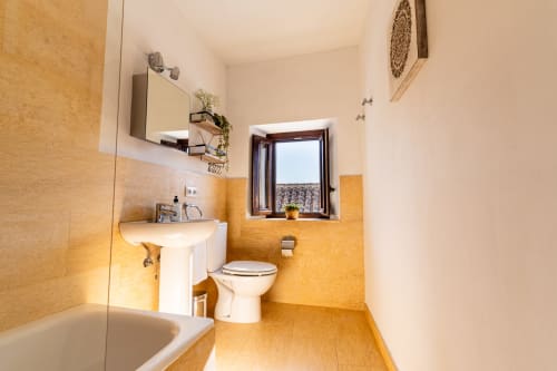 Baño luminoso en villa Casa de Medina, Medina Sidonia, con azulejos dorados, lavamanos blanco, inodoro, bañera y ventana