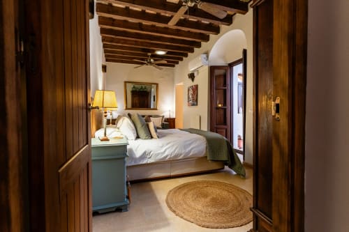Amplio dormitorio andaluz en la villa Casa de Medina, Medina Sidonia, con vigas de madera, mesita azul y alfombra de yute redonda