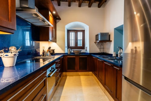 Cocina moderna con muebles de madera oscura, encimeras azules, electrodomésticos de acero inoxidable y arco en Casa de Medina
