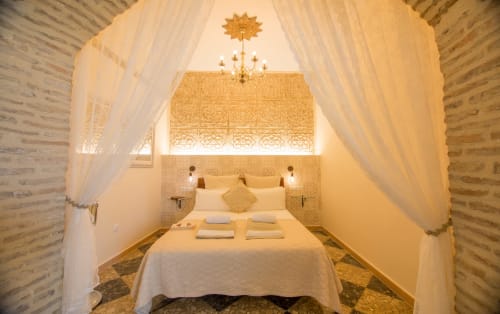 Dormitorio de lujo con cama dosel, cortinas color crema y cabecero dorado ornamentado en La Vista Medina Stays, Andalucía