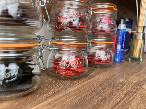 Le Lien 56 Vannes: Row of red Le Parfait preserving jars with clip-top lids on wooden shelf
