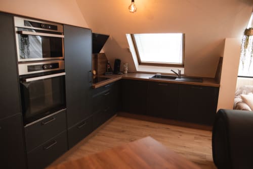 Modern attic kitchen with black cabinetry, wooden countertops, skylights, and integrated appliances at Love Room hotel in
