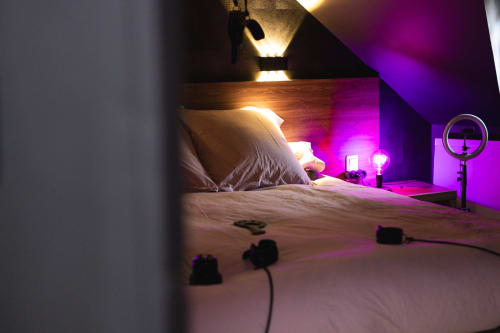 Modern bedroom with purple ambient lighting, bed with pillows, ring light setup, and cables at Love Room Le Lien 56 in Vannes