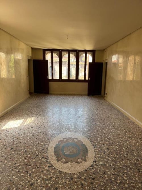 Stanza vuota con pavimento in terrazzo e stemma mosaico circolare presso Casanova Hideaway, Venezia