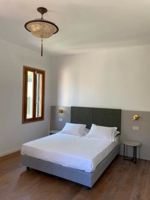 Camera moderna di Casanova Hideaway Venezia con testata verde, biancheria bianca, pavimento in legno e lampada a sospensione
