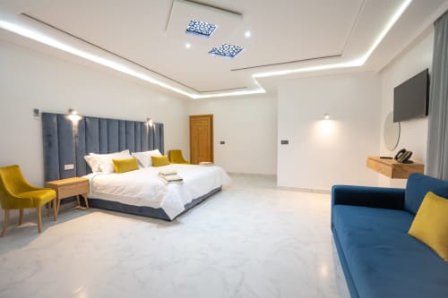 Luxury suite at Riad Gold Hôtel in Azrou with blue headboard bed, yellow accents, marble floor, and mountain views