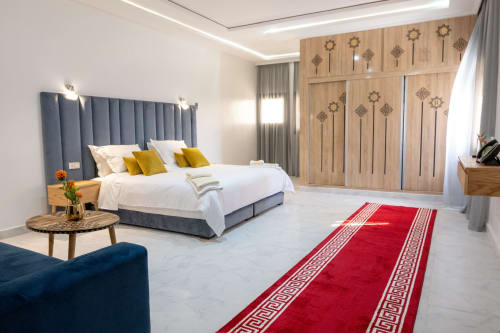 Luxury suite at Riad Gold Hôtel in Azrou with blue headboard bed, wooden wardrobe, red runner rug, and mountain views