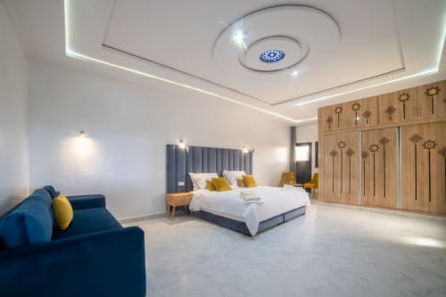 Modern luxury suite at Riad Gold Hôtel in Azrou with king bed, blue sofa, wooden wardrobe, and contemporary ceiling lights.