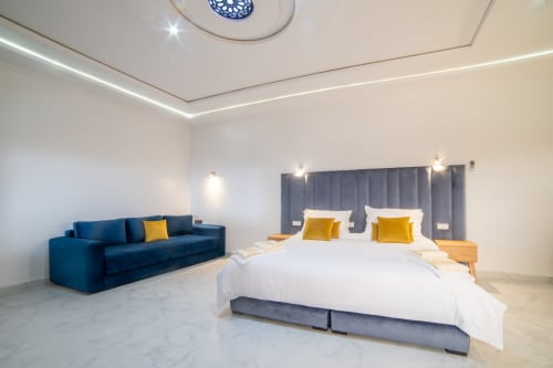 Modern suite at Riad Gold Hôtel in Azrou with blue velvet sofa, white bedding, yellow accents, and mountain views