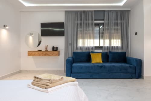 Modern family room at Riad Gold Hôtel in Azrou with blue sofa, flat-screen TV, wooden vanity, round mirror, and garden view