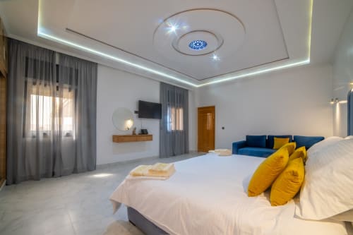 Spacious family room at Riad Gold Hôtel in Azrou with king bed, blue sofa, modern ceiling lights, and garden views through