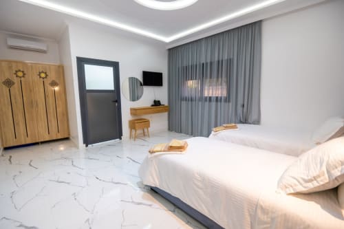 Modern double bedroom at Riad Gold Hôtel in Azrou with twin beds, wooden wardrobe, desk, flat-screen TV, and garden view