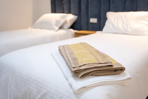 Folded towels with gold accents on white bedding in a Riad Gold Hôtel double room in Azrou