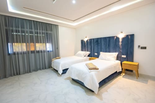 Modern twin bedroom at Riad Gold Hôtel in Azrou with blue upholstered headboards, white linens, and marble flooring.