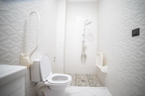 Modern bathroom at Riad Gold Hôtel in Azrou with white textured walls, toilet, shower, and pebble flooring