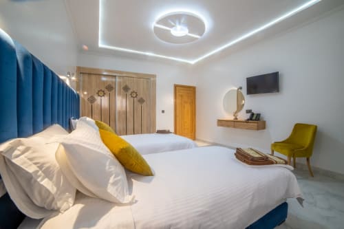 Modern double bedroom at Riad Gold Hôtel in Azrou with blue headboard, white bedding, and contemporary ceiling lights