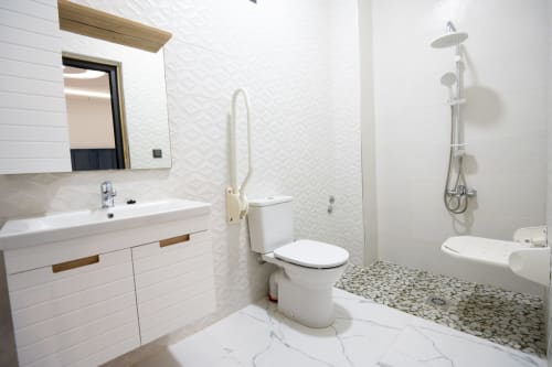 Modern accessible bathroom in Riad Gold Hôtel Azrou with white sink, toilet, walk-in shower with handheld showerhead, and