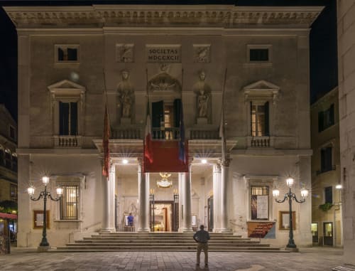 Facciata storica di palazzo veneziano illuminato di notte con colonne classiche e statue