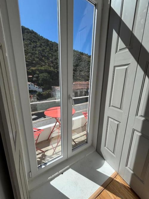 Glass doors opening to balcony with red chairs overlooking forested mountains at Casa Tawny, Pinhão