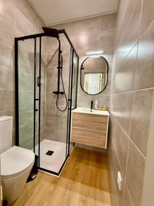 Modern bathroom at Casa Tawny in Pinhão with black-framed shower enclosure, wooden vanity, oval mirror, and tiled walls