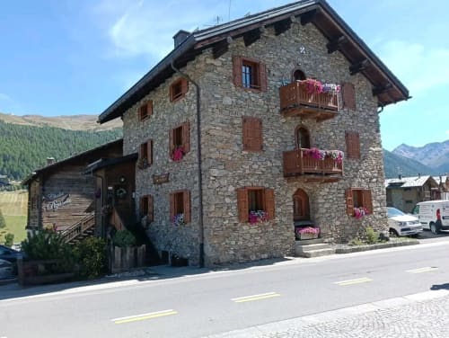 Edificio in pietra Al Dos a Livigno con balconate in legno, fioriere e Alpi sullo sfondo
