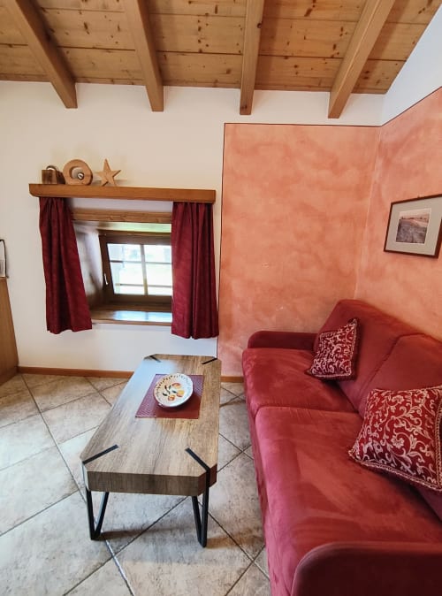 Accogliente soggiorno dell'appartamento Al Dos a Livigno con divano rosso, travi in legno e vista sulle montagne