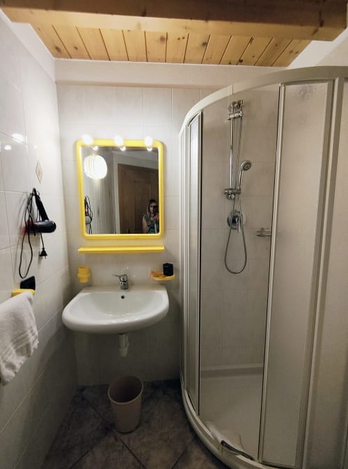 Bagno moderno nell'appartamento di montagna Al Dos a Livigno con specchio a cornice gialla, lavabo bianco e cabina doccia in vetro
