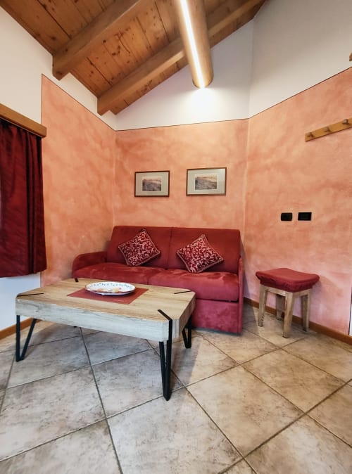 Accogliente soggiorno dell'appartamento Al Dos a Livigno con divano rosso, tavolo in legno e pareti color terracotta