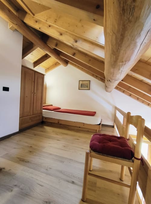 Camera da letto in stile rustico presso Al Dos Livigno con travi in legno a vista, letto singolo con cuscino bordeaux e appartamento di montagna