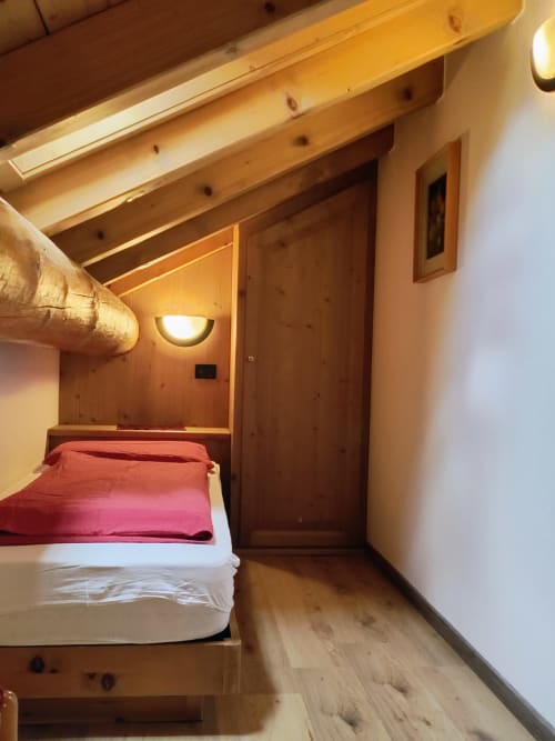 Camera da letto in legno accogliente dell'appartamento Al Dos a Livigno con biancheria rossa e illuminazione soffusa