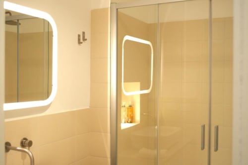 Bagno moderno con specchio illuminato, cabina doccia in vetro e piastrelle color crema presso Le Dimore Del Duca Roma