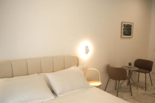 Camera da letto moderna a Le Dimore Del Duca Roma con testata imbottita beige, biancheria bianca, lampada murale rotonda e