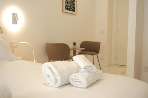 Asciugamani bianchi arrotolati sul letto in moderna camera d'hotel a Roma con sedie marroni e lampada da tavolo