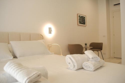 Camera da letto moderna e doppia presso Le Dimore Del Duca Roma con letto color crema, asciugamani arrotolati, illuminazione contemporanea e zona living marrone