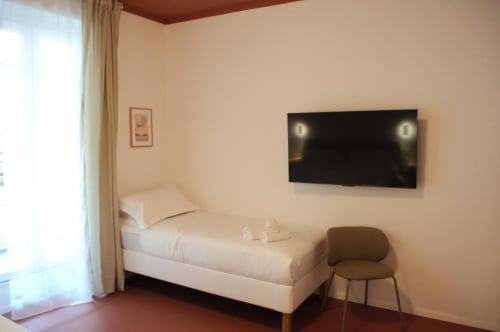 Camera moderna a Le Dimore Del Duca Roma con letto singolo, TV a parete, poltrona marrone e porta finestra in vetro