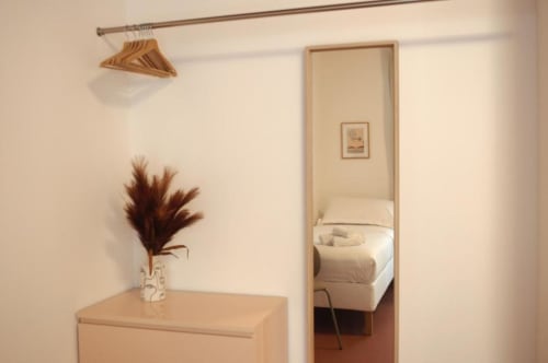 Ingresso minimalista a Le Dimore Del Duca Roma con appendiabiti in legno, fiori secchi e vista riflessa della camera da letto