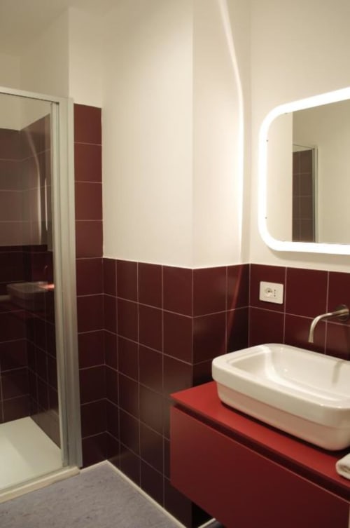 Bagno moderno al Le Dimore Del Duca Roma con piastrelle bordeaux, lavabo bianco, specchio illuminato e doccia aperta