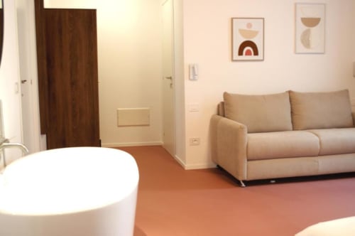 Camera moderna a Le Dimore Del Duca Roma con divano letto beige, tavolo rotondo bianco e arte geometrica a parete che affaccia sulla corte