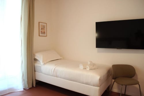 Camera moderna del Le Dimore Del Duca Roma con letto singolo, TV a schermo piatto, poltrona e arredamento minimalista a Roma