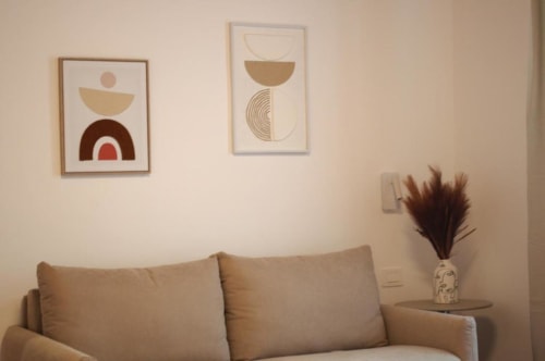 Divano beige con cuscini nella camera d'hotel Roma, con arte geometrica astratta alle pareti e vaso decorativo con fiori secchi