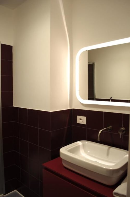 Bagno moderno del Le Dimore Del Duca Roma con piastrelle nere, lavabo bianco a vessel, specchio illuminato e piano rosso.