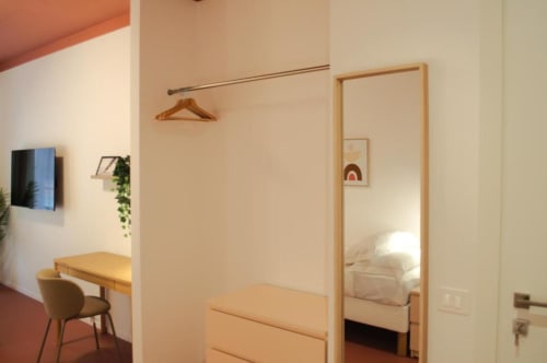 Camera tripla moderna a Le Dimore Del Duca Roma con scrivania in legno, specchio, attaccapanni e letto visibile attraverso la porta