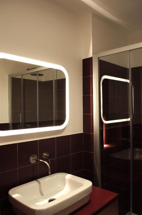 Bagno moderno presso Le Dimore Del Duca Roma con specchio illuminato, lavabo bianco, pareti in piastrelle scure e doccia in vetro