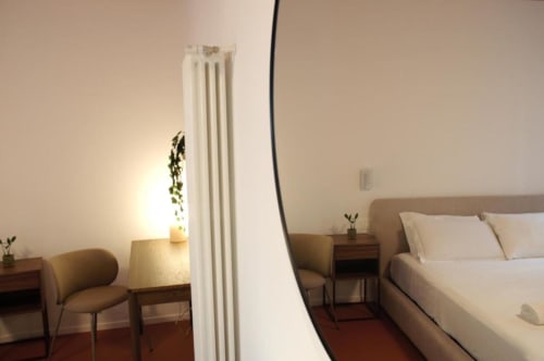 Camera moderna a Le Dimore Del Duca Roma con letto matrimoniale, comodini in legno, sedia scrivania, radiatore bianco e illuminazione calda